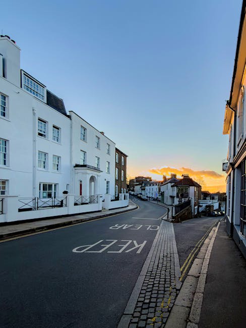 An empty residential street in Wealdstone during sunset, with a slight incline and narrow roadway. On the left side, there are white multi-storey buildings with windows and small railings, indicating